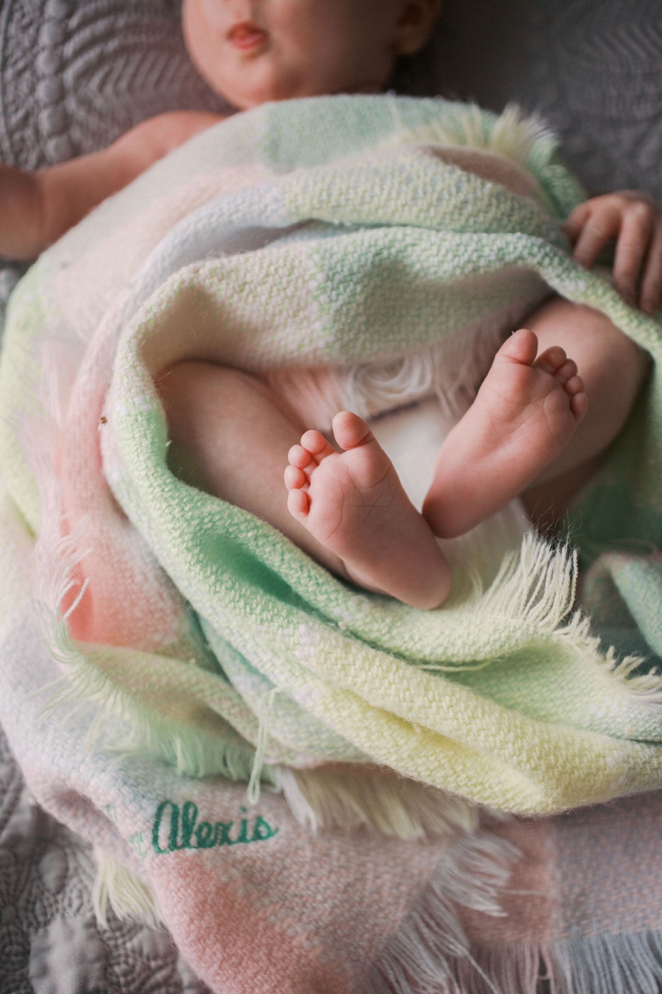 Newborn's bare feet peek from soft pastel blanket while swaddled peacefully during intimate in-home session