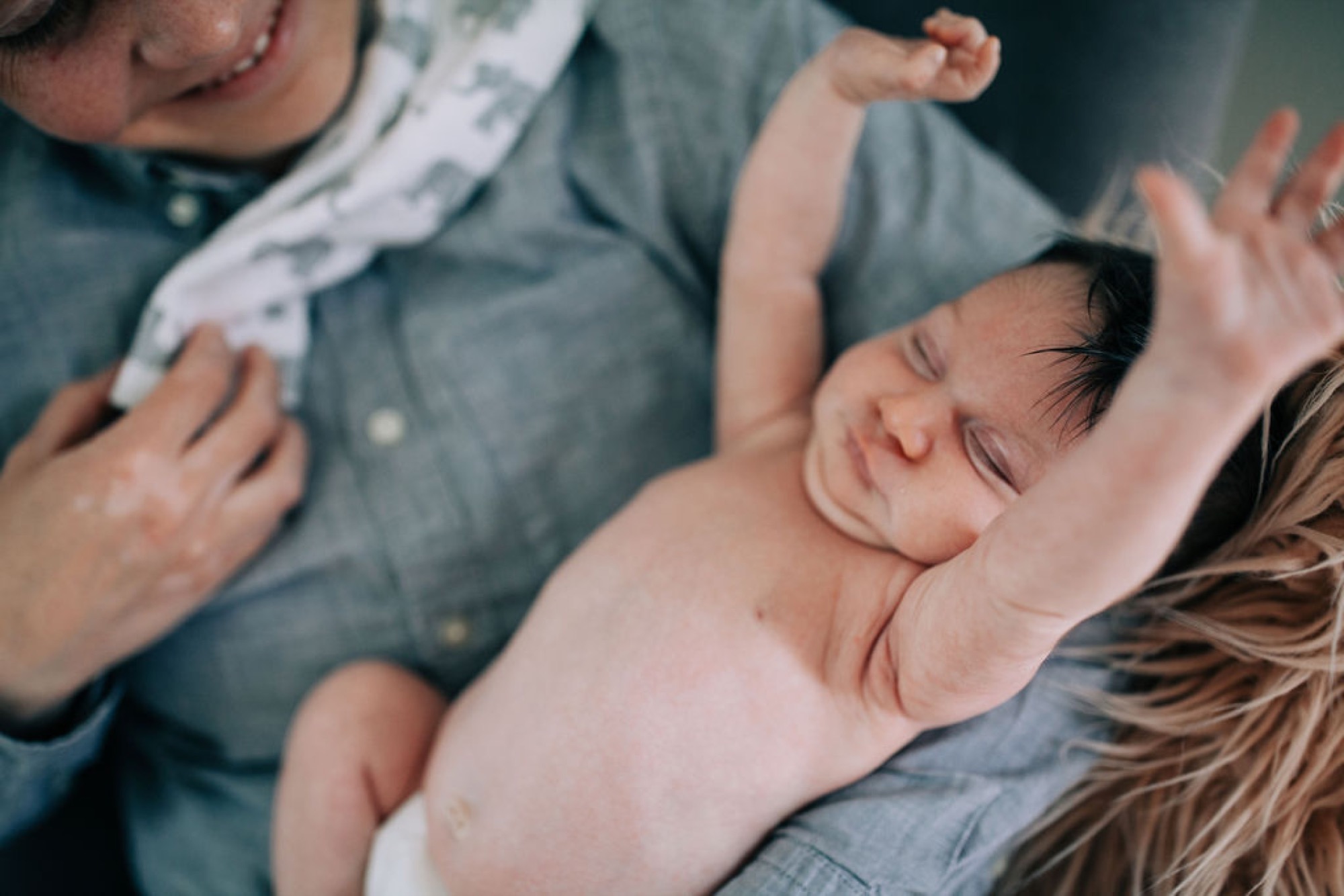 Newborn sleeps peacefully in mother's arms while father and sibling lean in close, dressed in coordinating denim for an intimate family moment