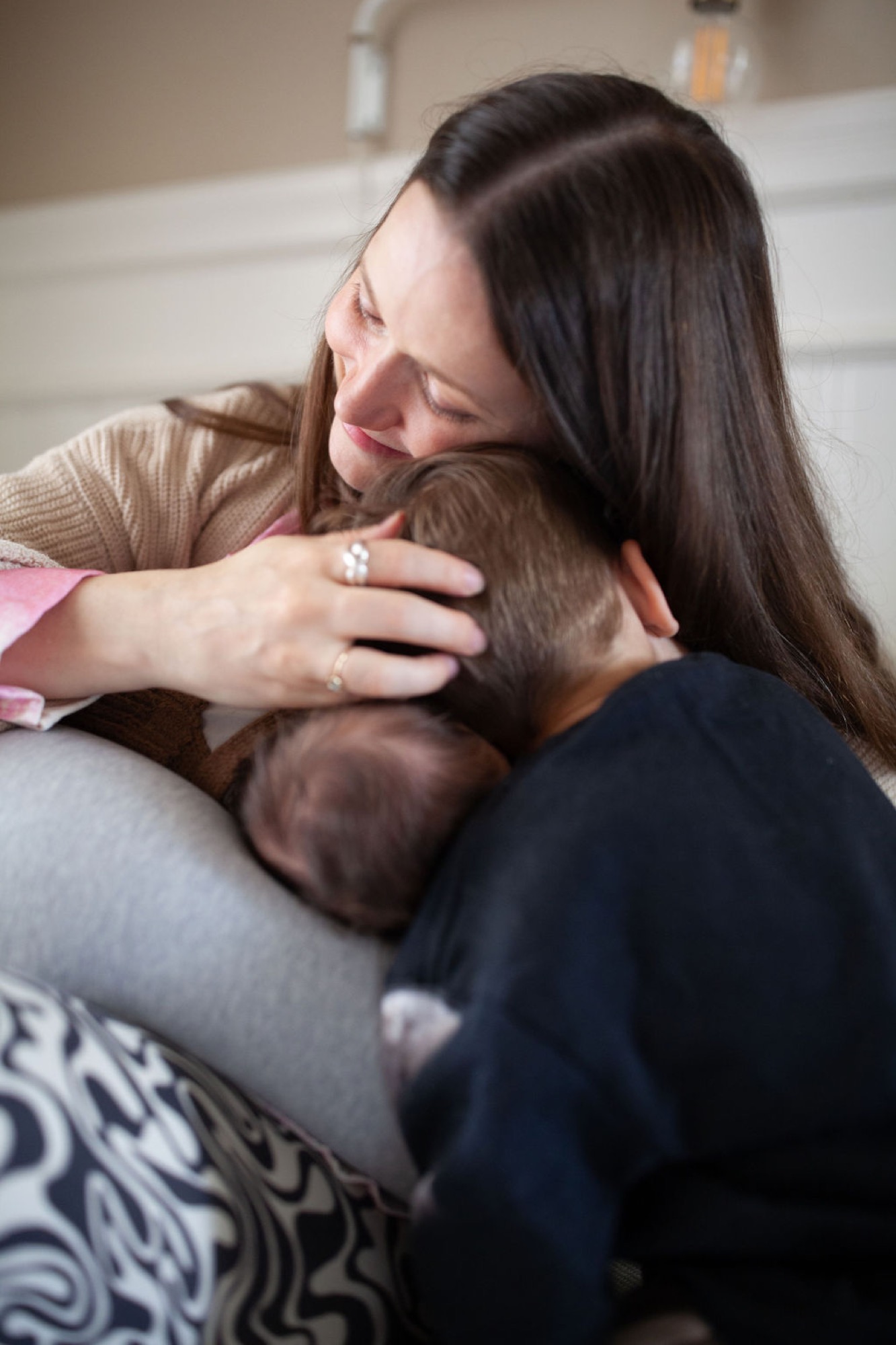 Mother gazes down tenderly at her newborn cradled against her chest in a soft indoor setting