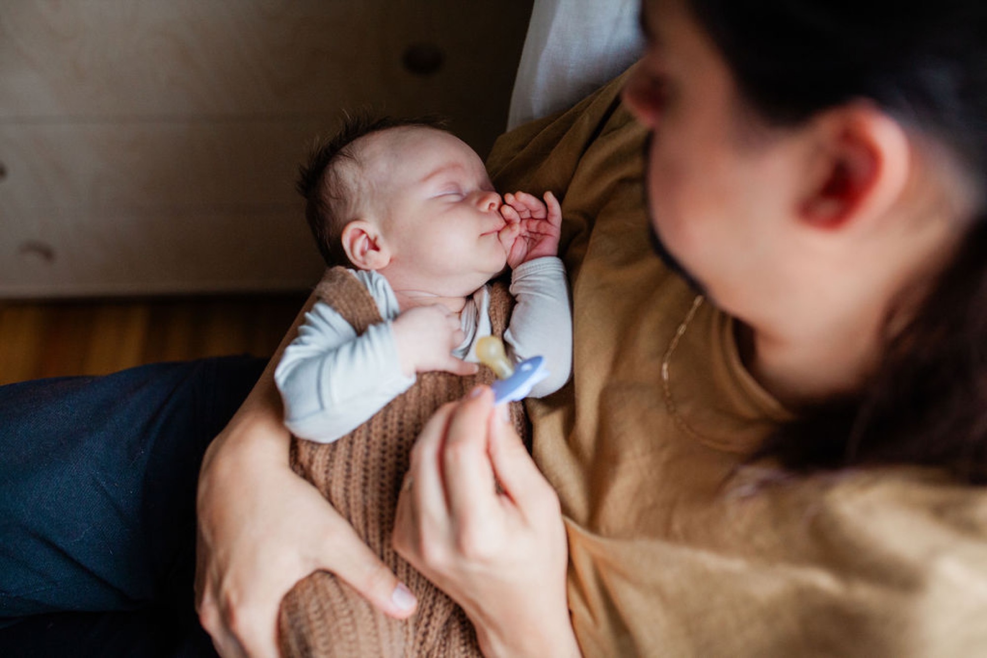 A parent gazes down at their sleeping newborn swaddled in a tan blanket during an intimate indoor moment