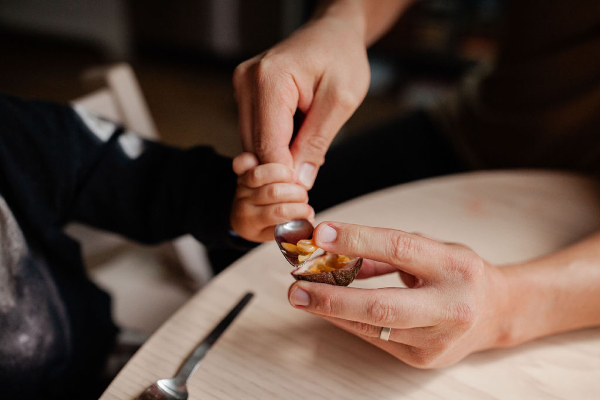 Two small hands exchange a handful of mixed nuts on a wooden surface during an intimate indoor moment