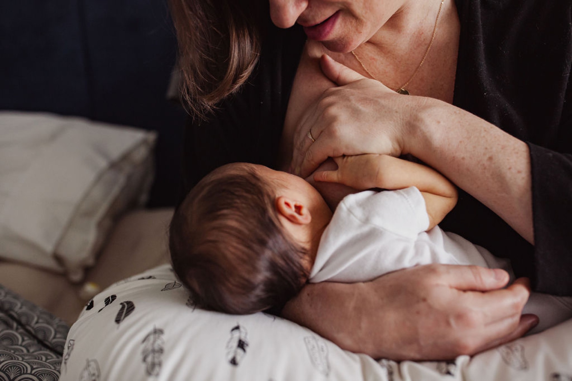 A mother gazes down tenderly at her newborn during an intimate bedside moment, soft natural light illuminating their connection