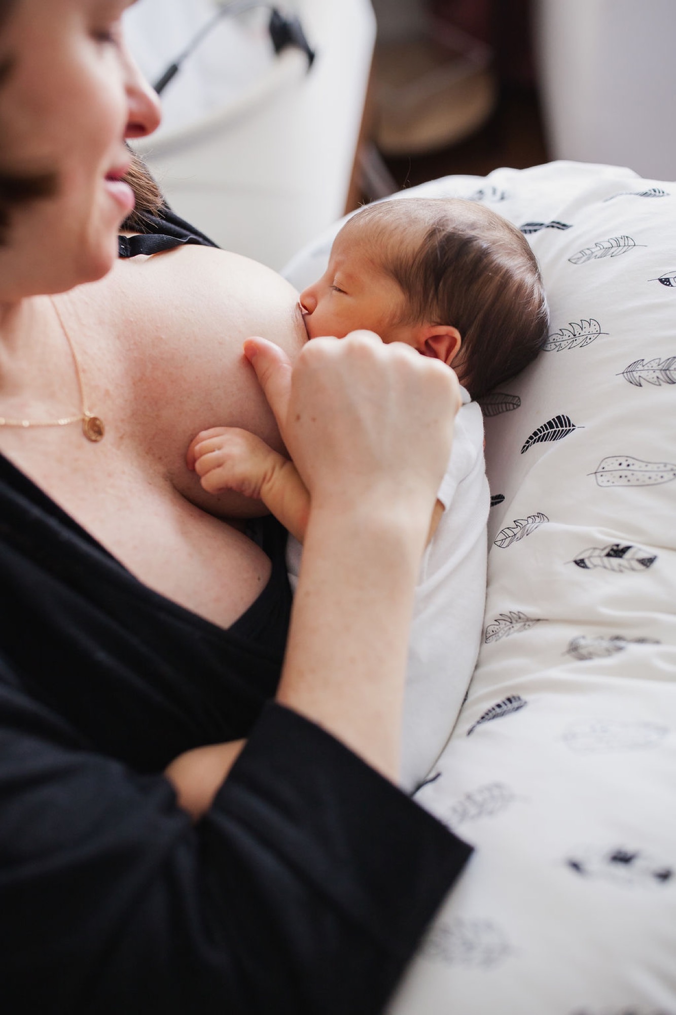 Mother gazes down at her peacefully sleeping newborn nestled against her chest in soft natural light