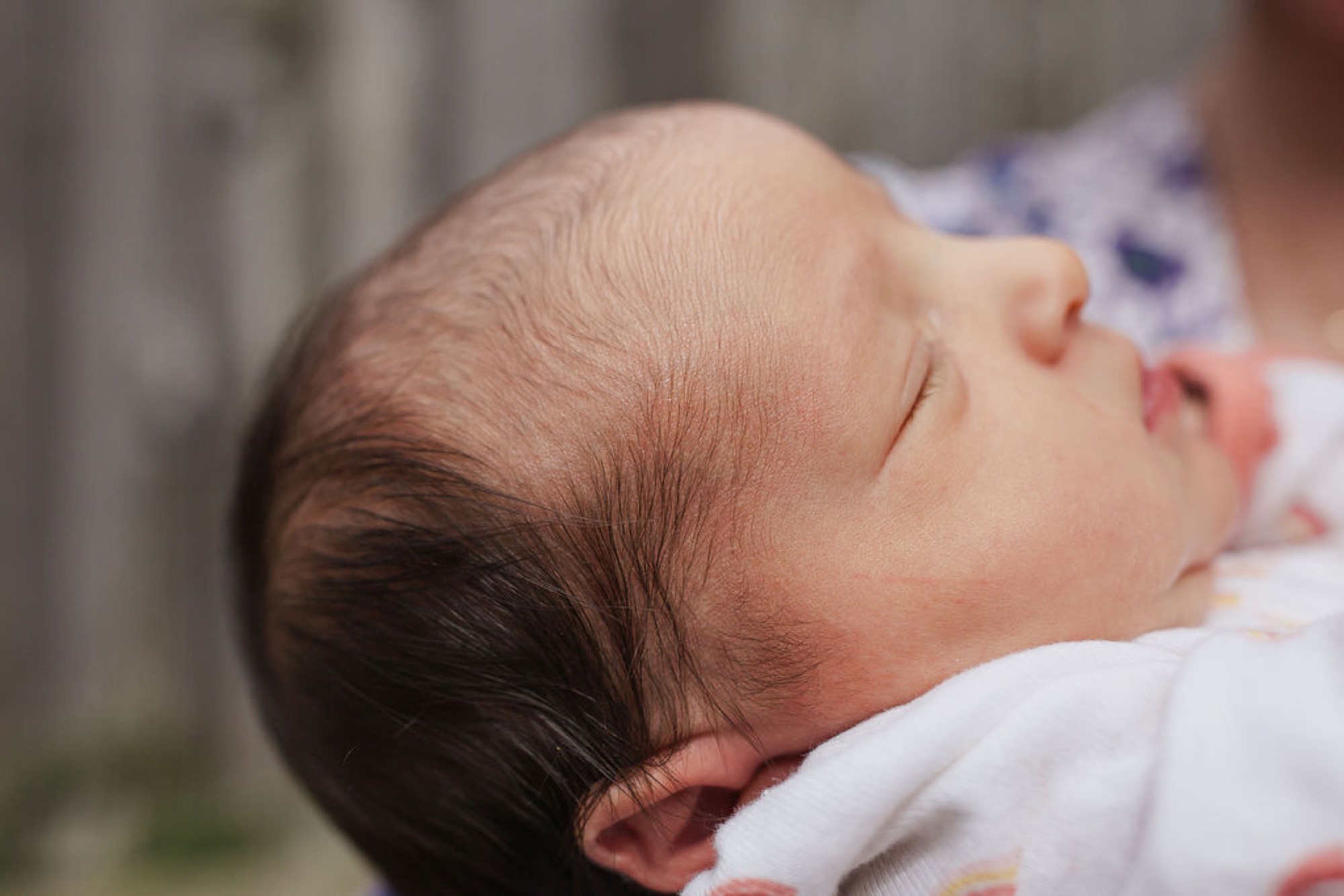 Newborn sleeps peacefully in profile against white fabric, dark hair catching soft indoor light