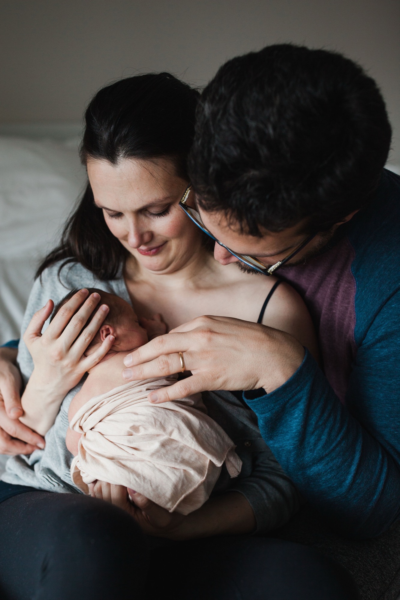 Father gazes down at newborn cradled in mother's arms, intimate moment bathed in soft natural light