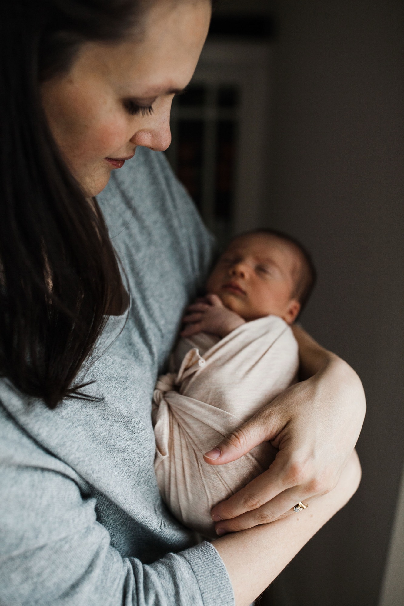 Mother gazes down at her swaddled newborn in soft natural light, cradling the infant close to her chest