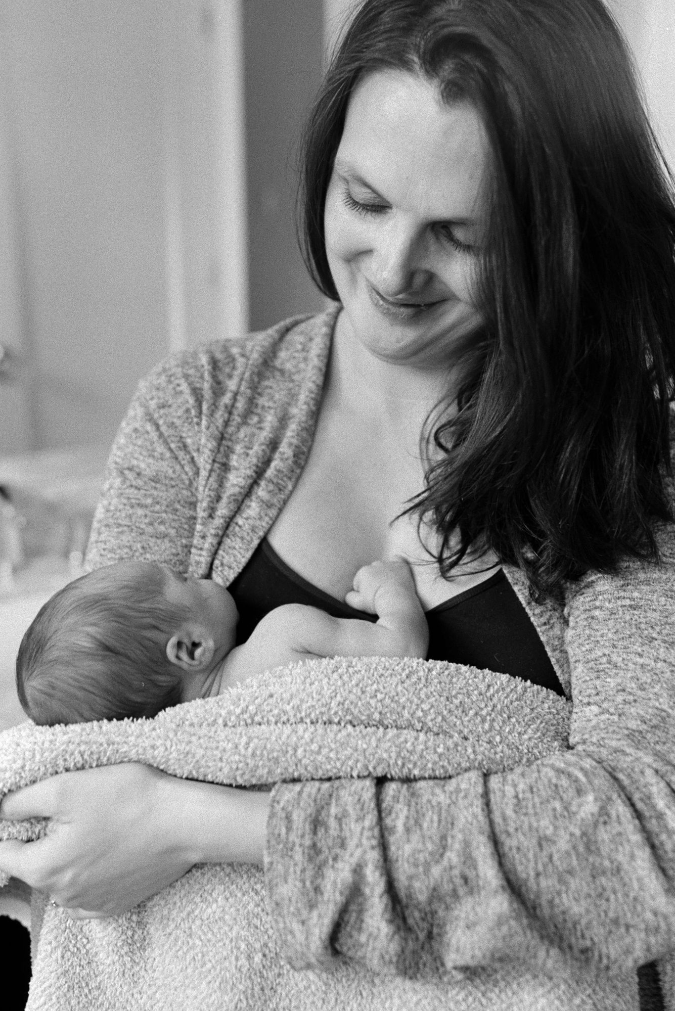 A mother gazes down at her nursing newborn with a warm, tender smile in soft natural light