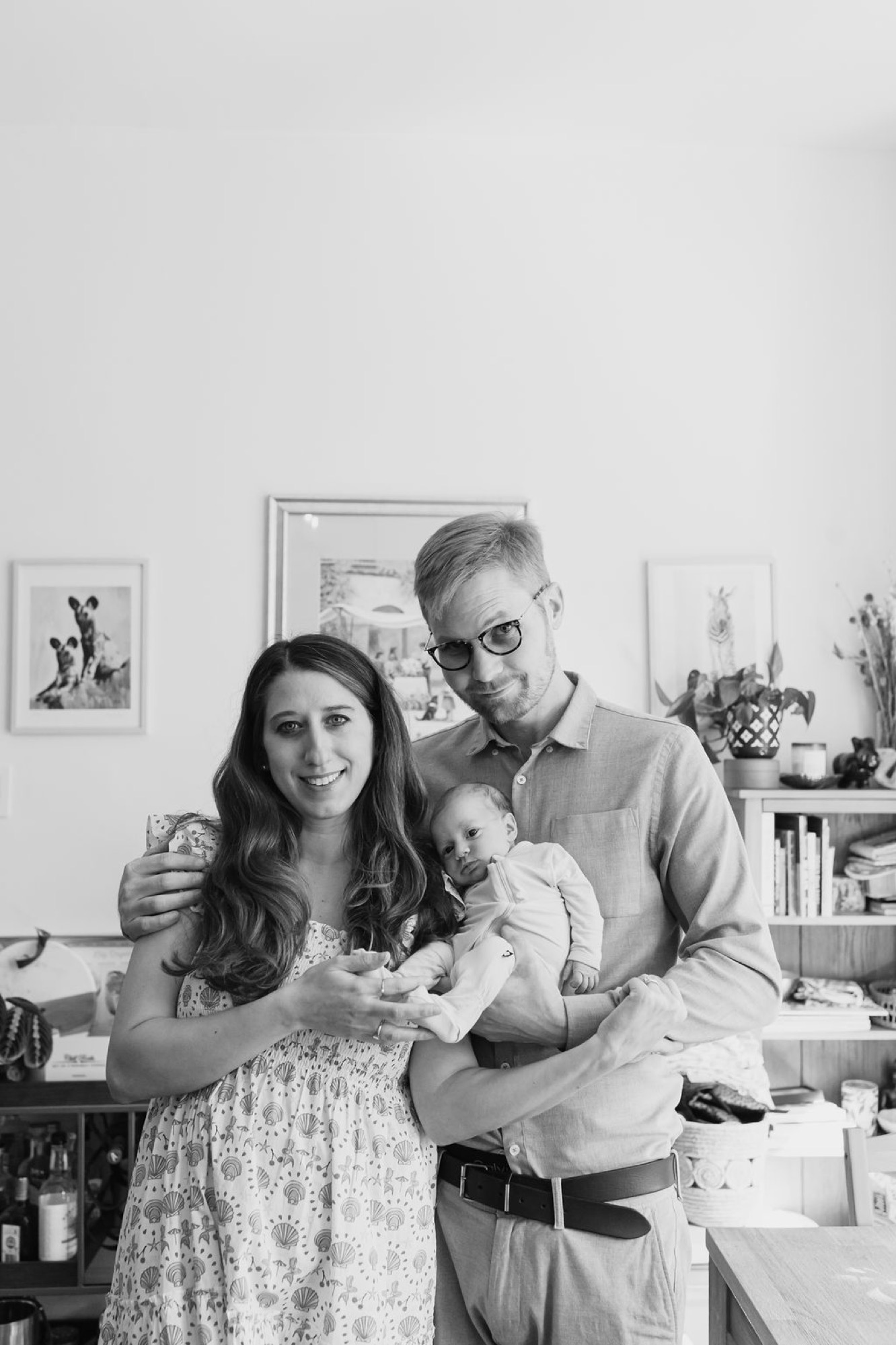 A young family stands together in a bright kitchen, the father holding their newborn while the mother smiles warmly beside them